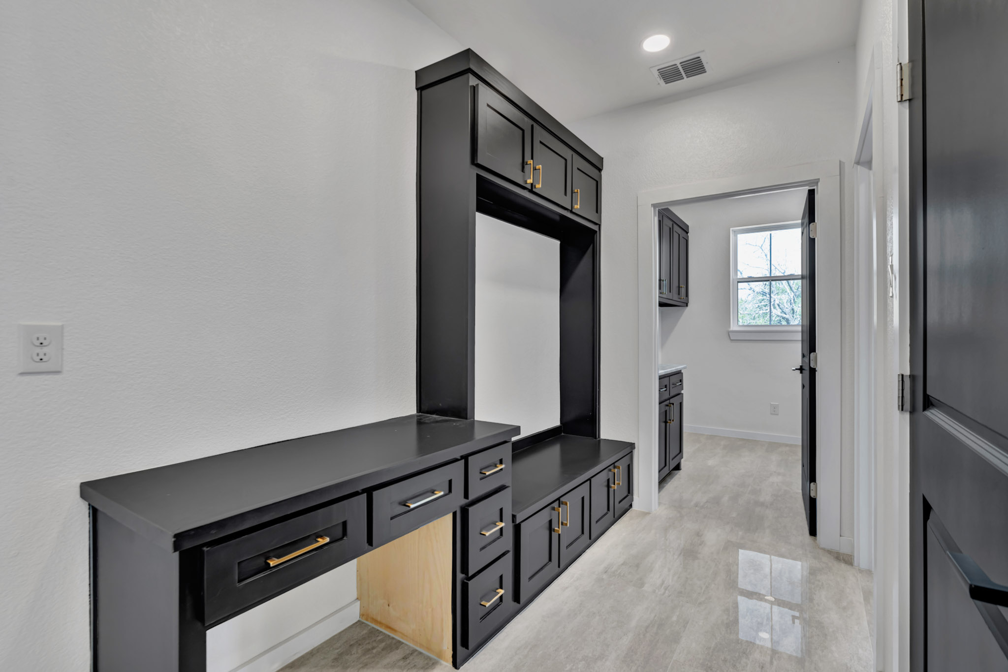 Mudroom drop zone with a black built in bench, desk and upper cabinets