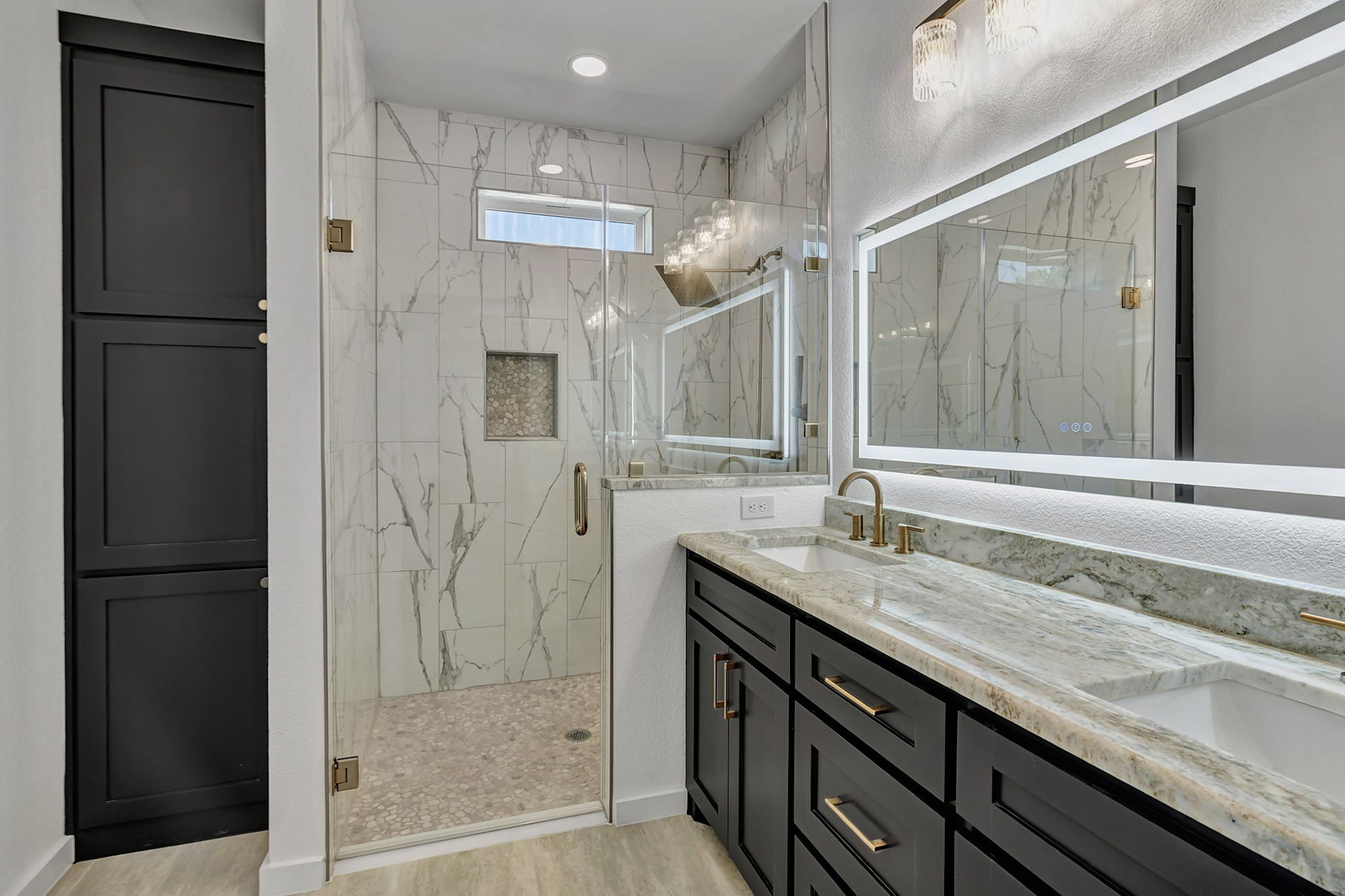 Primary bath with a marble tile shower, frameless glass and a double vanity