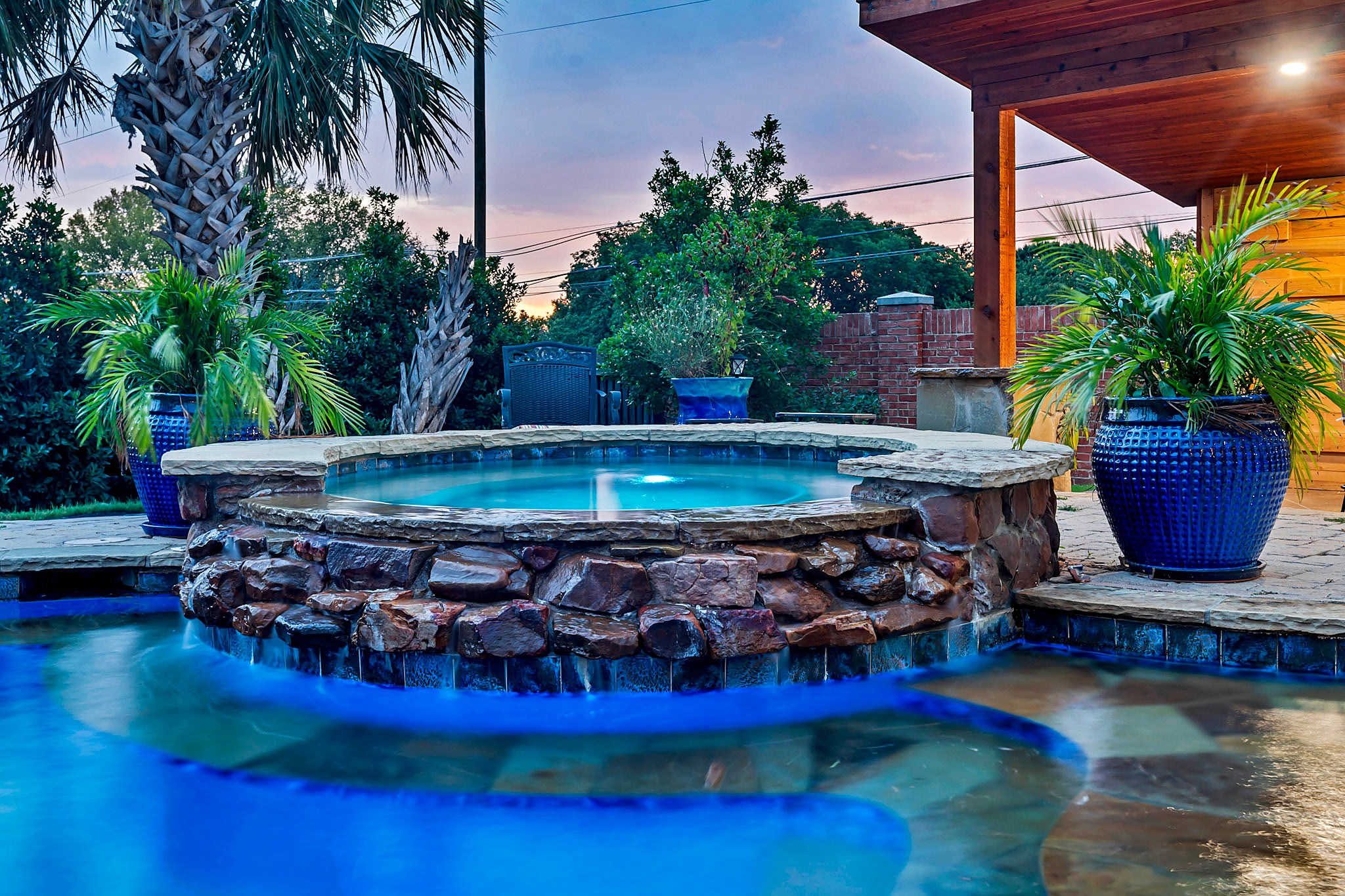 Lit spa spilling over a stone wall into the pool
