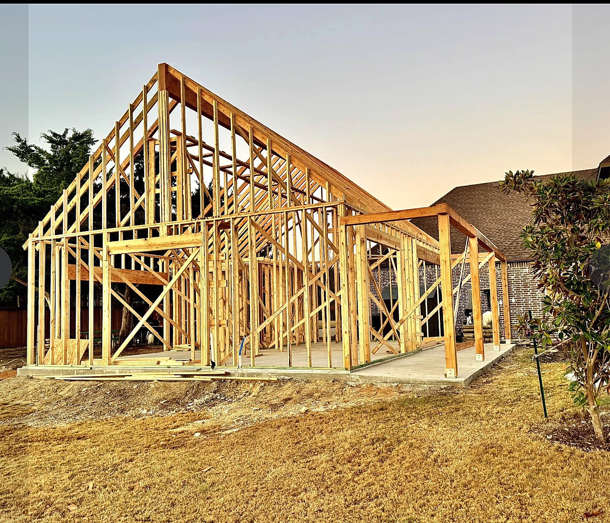 Stick framed garage and shop addition going up beside a brick home